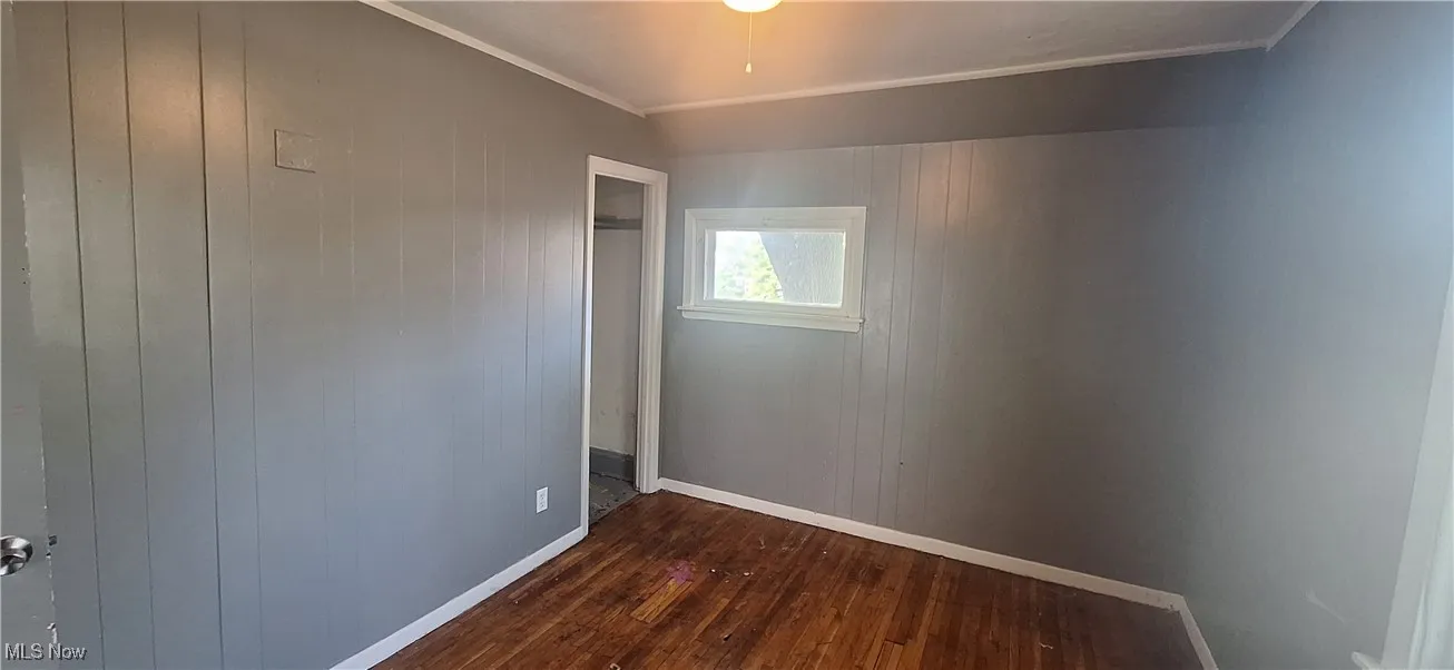 Empty room with crown molding, dark wood-style flooring, baseboards, and wood walls