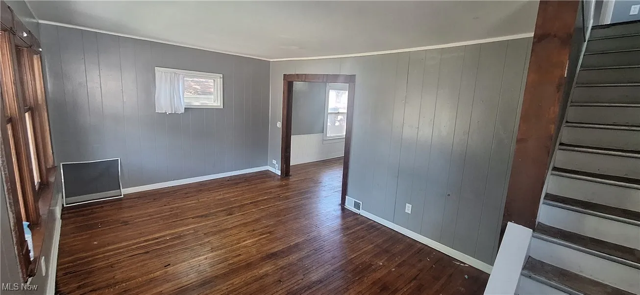 Unfurnished room with baseboards, wood walls, dark wood-style floors, and stairway