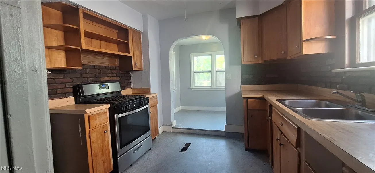 Kitchen with open shelves, a sink, decorative backsplash, and stainless steel gas range oven
