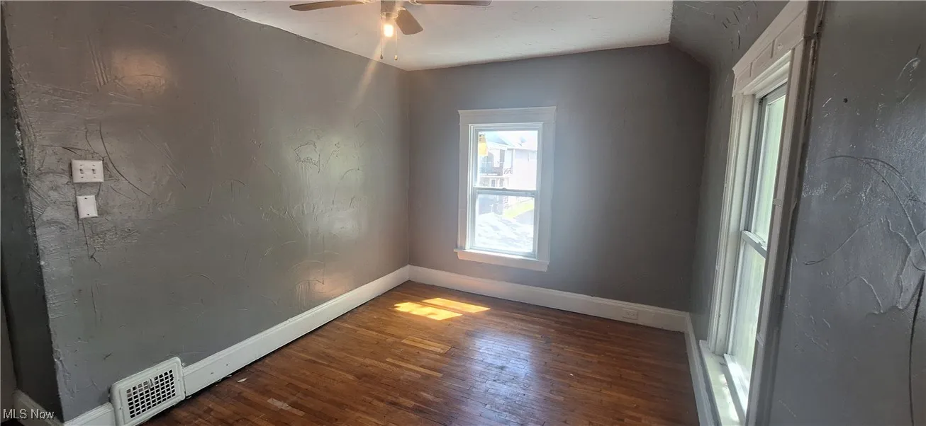 Spare room with ceiling fan, visible vents, vaulted ceiling, hardwood / wood-style flooring, and baseboards
