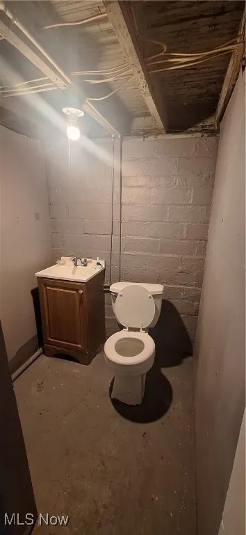 Bathroom with toilet, concrete block wall, unfinished concrete flooring, and a sink