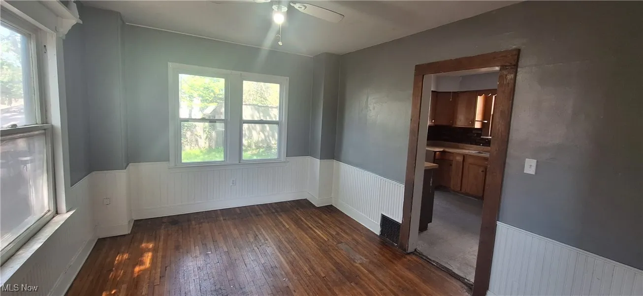Empty room featuring wood-type flooring, ceiling fan, and a wainscoted wall