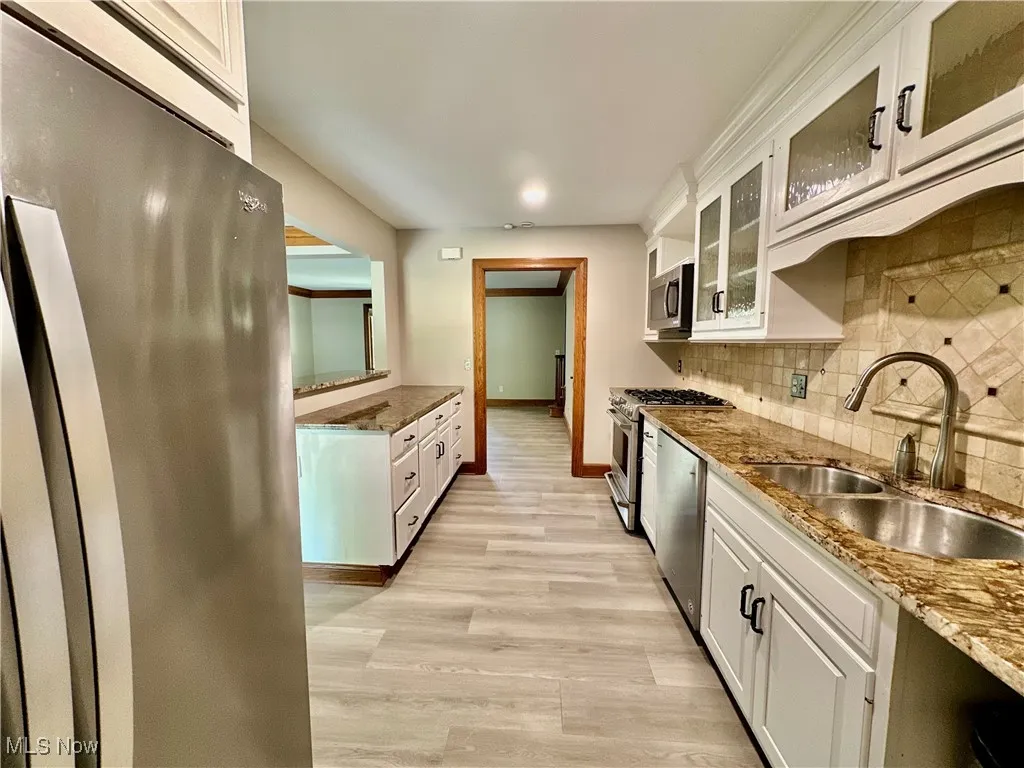 Kitchen featuring stainless steel appliances, tasteful backsplash, white cabinetry, light wood-type flooring, and glass insert cabinets