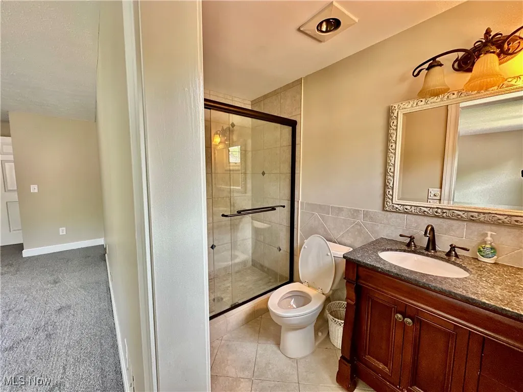 Full bath featuring a shower stall, vanity, tile patterned floors, and tile walls