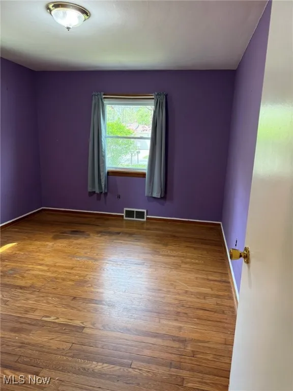 Unfurnished room with baseboards, visible vents, and wood finished floors