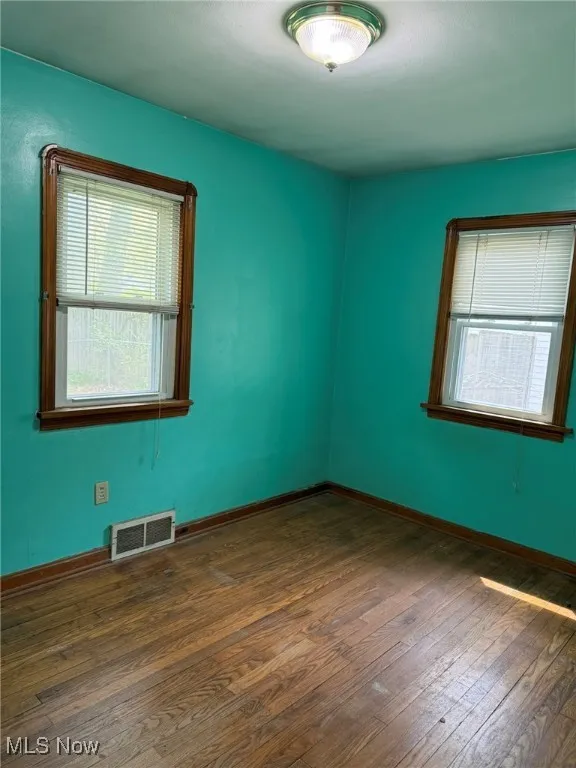 Empty room featuring baseboards, dark wood finished floors, and visible vents