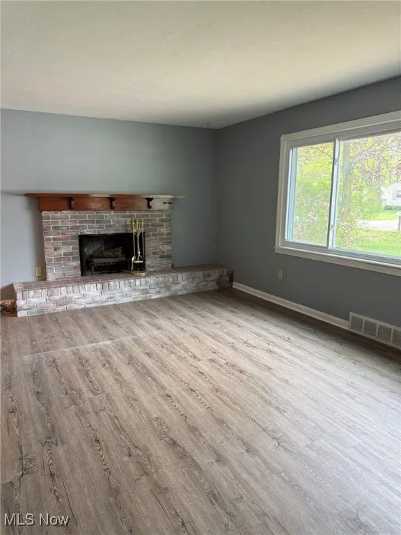 Unfurnished living room featuring visible vents, baseboards, wood finished floors, and a fireplace