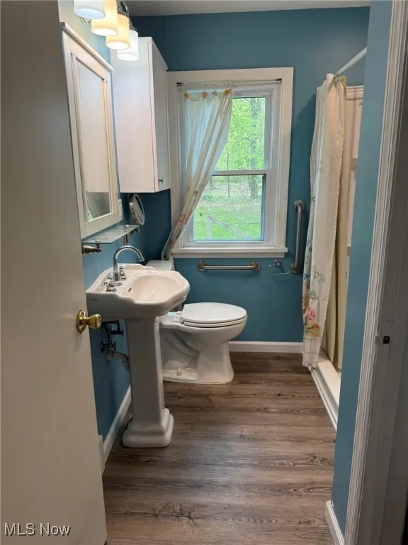 Full bath with toilet, baseboards, curtained shower, and wood finished floors
