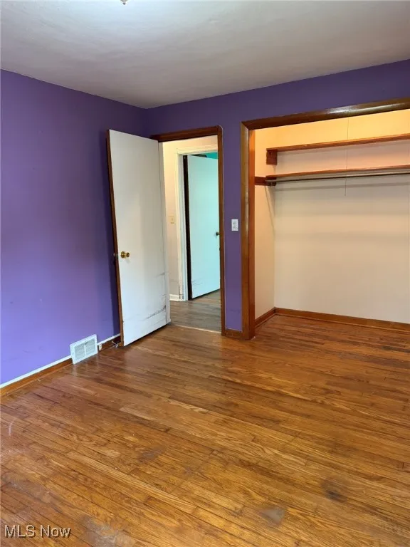 Unfurnished bedroom with a closet, baseboards, visible vents, and hardwood / wood-style floors