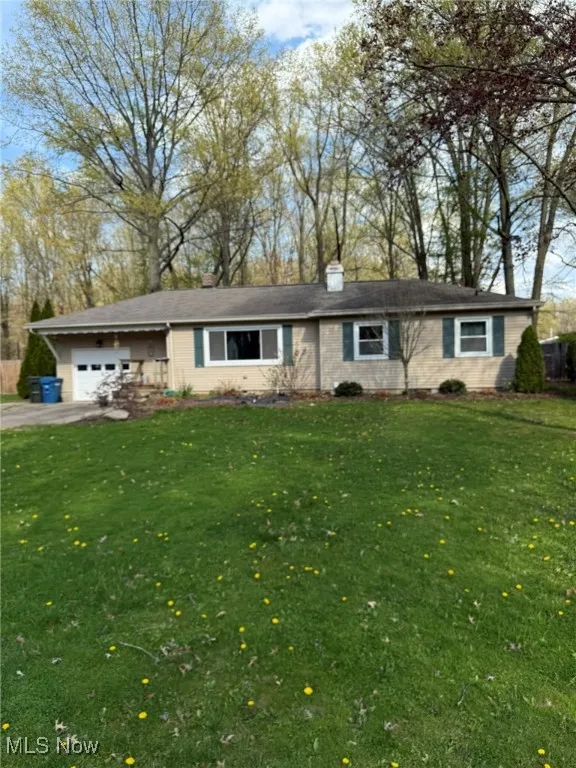 Ranch-style house featuring a chimney, an attached garage, driveway, and a front yard