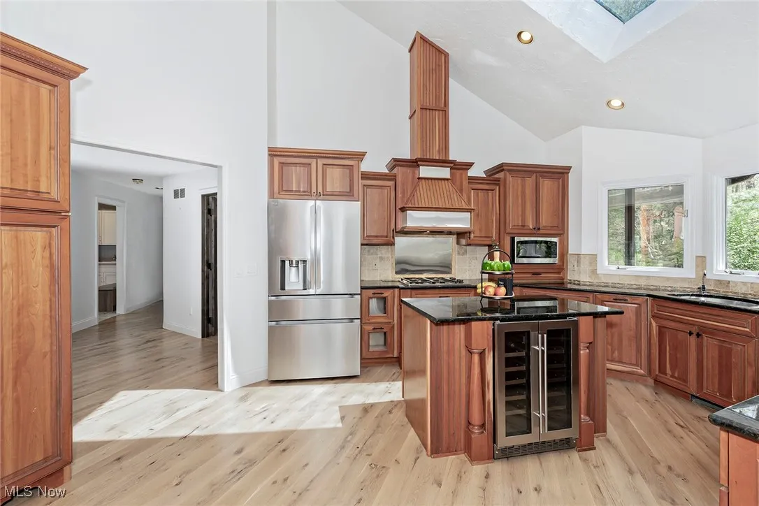 Another view of the Kitchen shows the LG stainless steel refrigerator, and custom stainless-trimmed hood fan and backsplash, underneath a skylit vaulted ceiling.