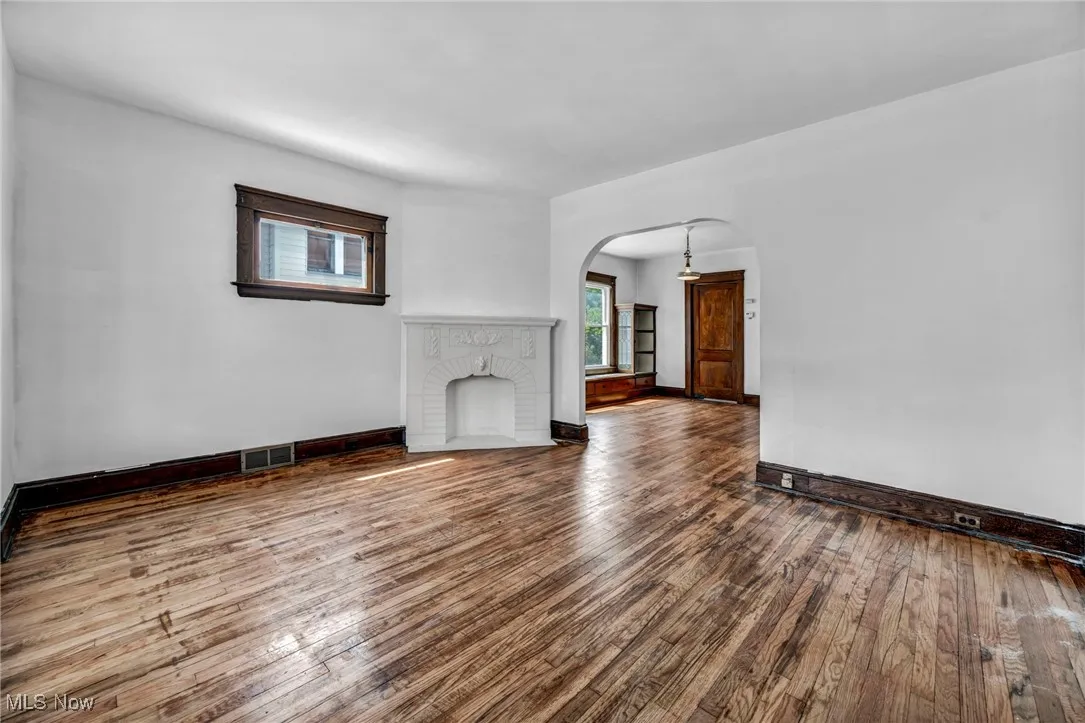 Unfurnished living room with a fireplace, wood-type flooring, arched walkways, baseboards, and visible vents
