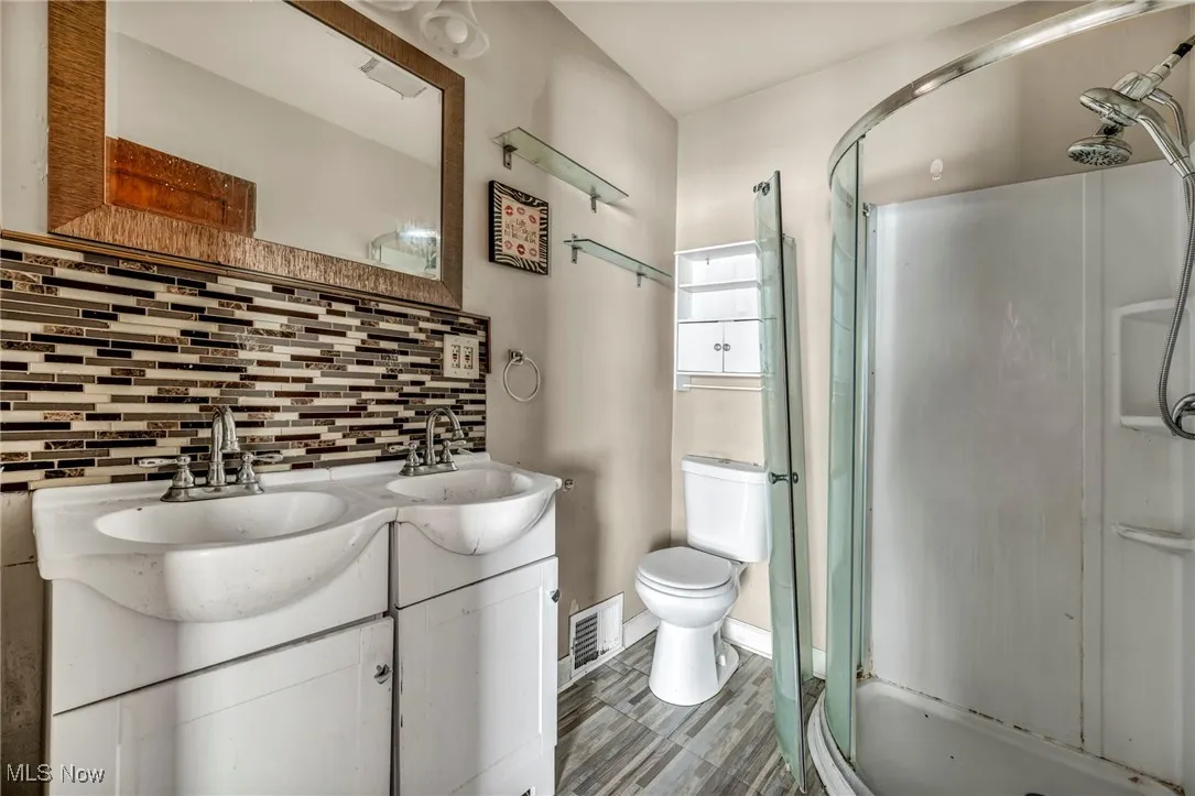 Full bathroom featuring a sink, double vanity, toilet, decorative backsplash, and a stall shower
