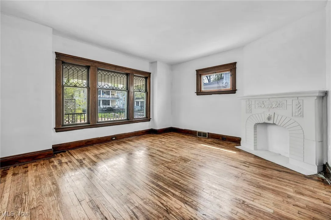 Unfurnished living room featuring a brick fireplace, baseboards, visible vents, and hardwood / wood-style flooring