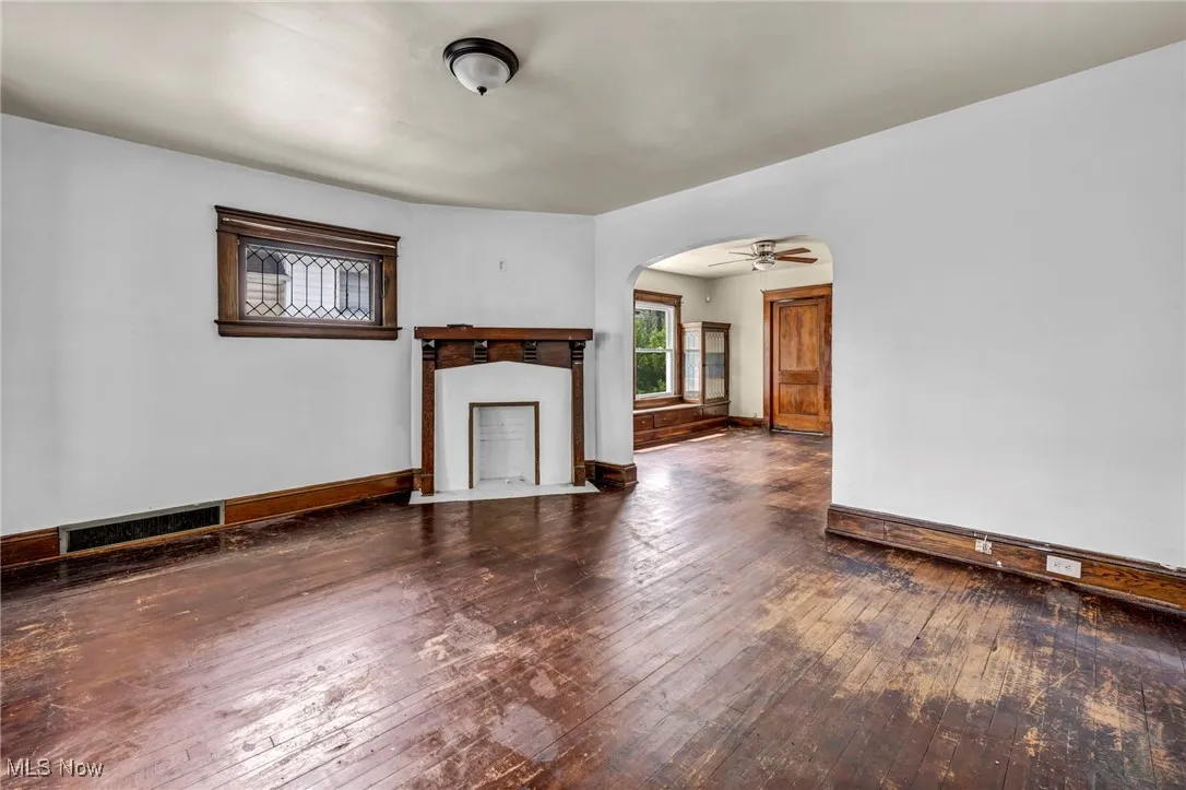 Unfurnished living room featuring visible vents, arched walkways, baseboards, and hardwood / wood-style flooring