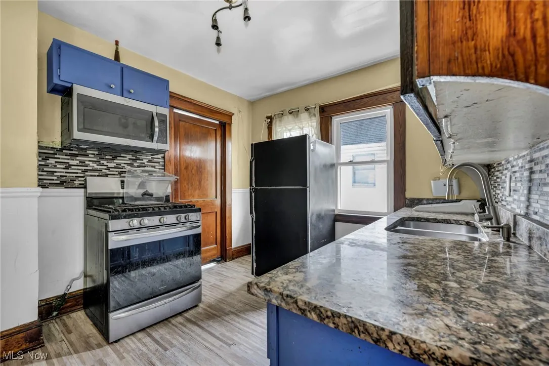 Kitchen with appliances with stainless steel finishes, a sink, light wood-style floors, blue cabinetry, and tasteful backsplash