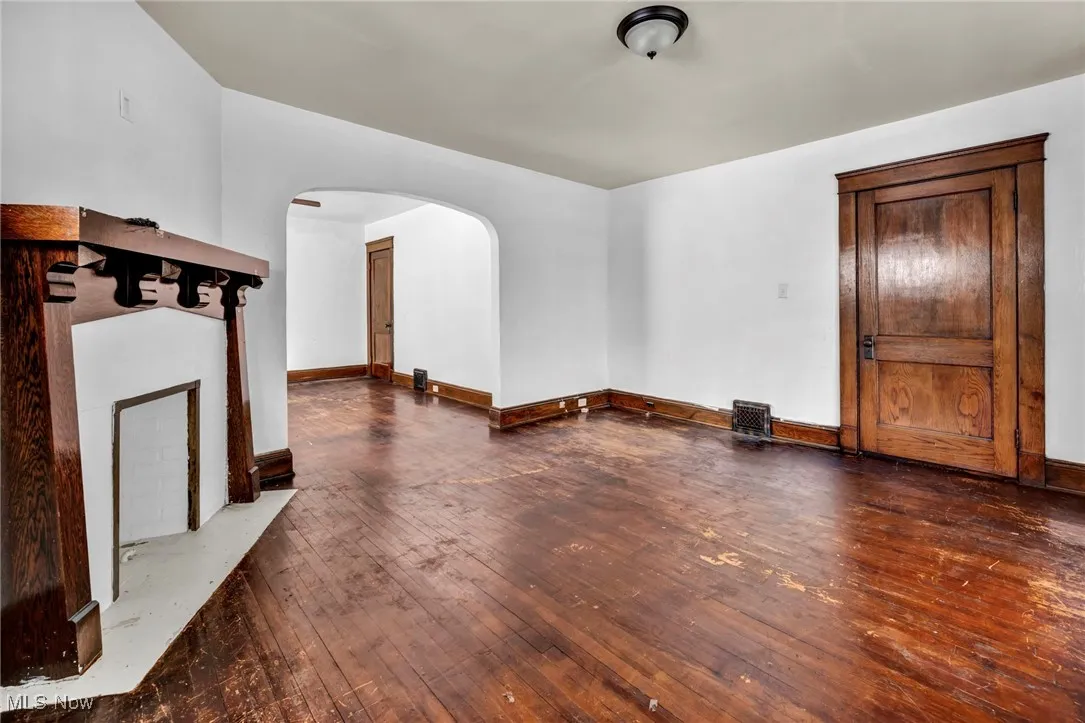 Unfurnished living room with arched walkways, baseboards, and hardwood / wood-style flooring