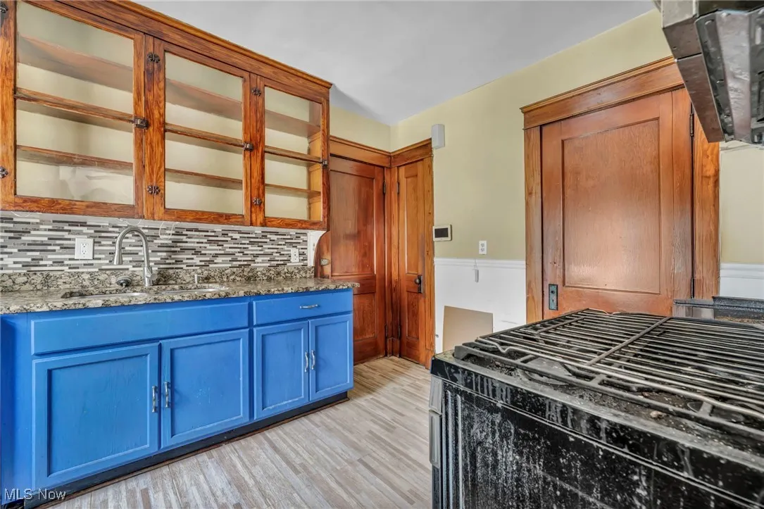 Kitchen with blue cabinets, tasteful backsplash, light wood-type flooring, a sink, and stone countertops