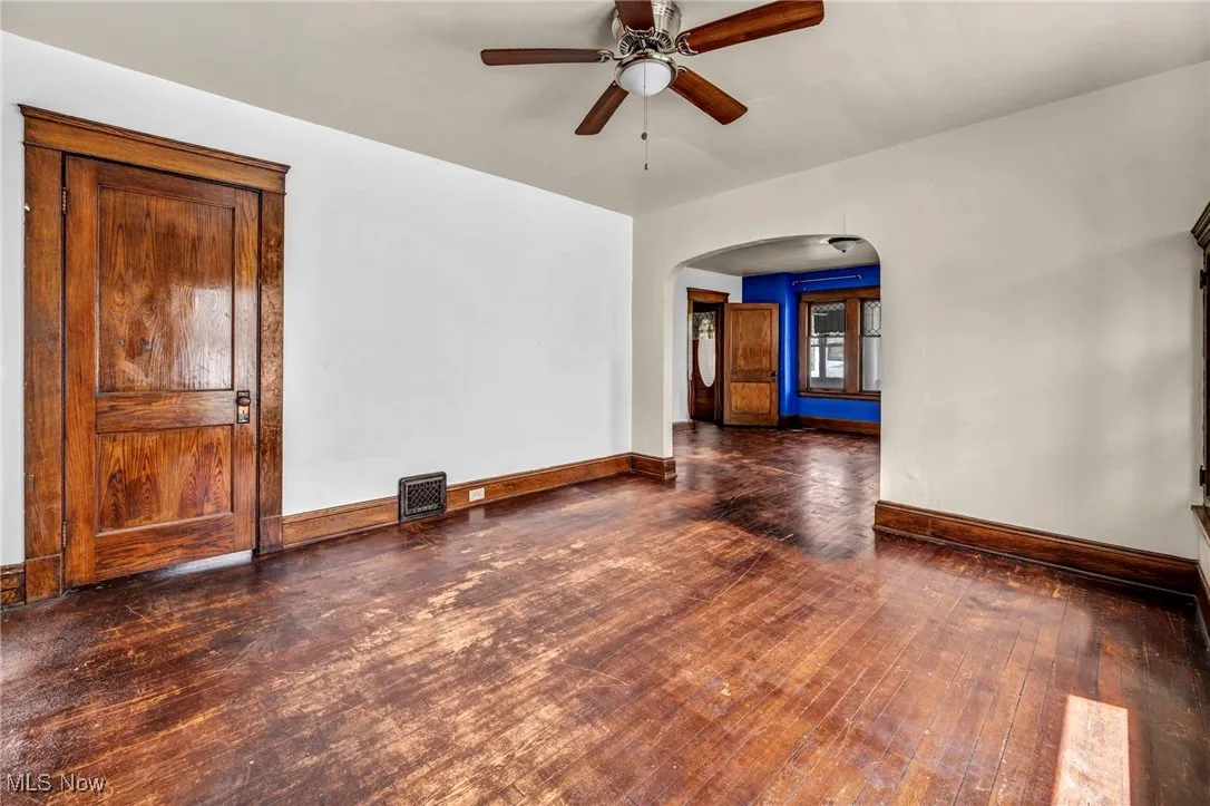 Empty room featuring ceiling fan, arched walkways, hardwood / wood-style floors, baseboards, and visible vents