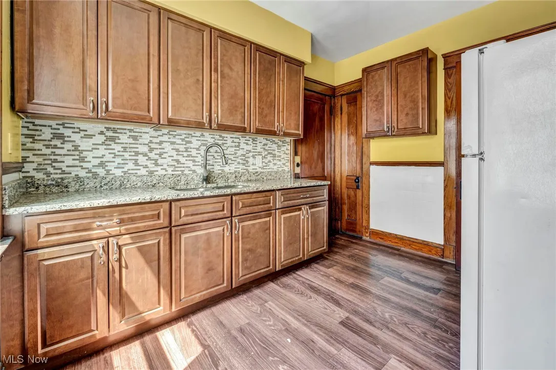 Kitchen featuring decorative backsplash, freestanding refrigerator, light wood-style floors, light stone counters, and a sink
