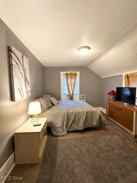 Bedroom with a textured ceiling, vaulted ceiling, and baseboards