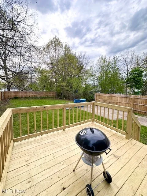 Wooden terrace featuring a fenced backyard, a lawn, and a grill