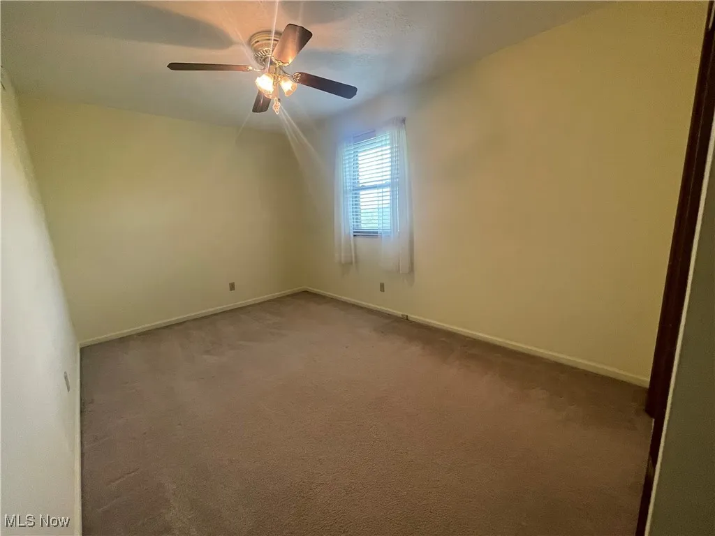 Carpeted spare room featuring baseboards and a ceiling fan