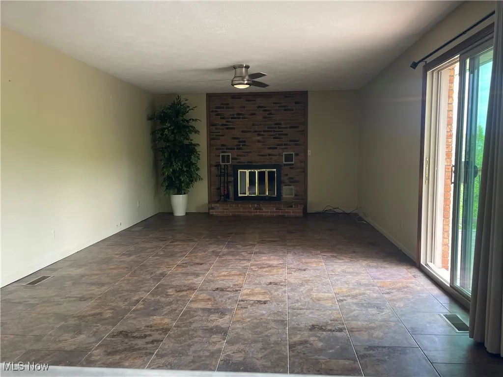 Unfurnished living room featuring baseboards, a ceiling fan, a brick fireplace, and visible vents