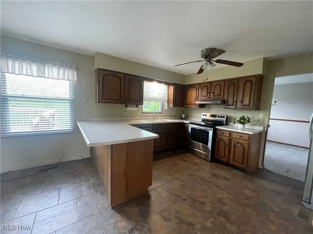 Kitchen with electric range, a peninsula, light countertops, under cabinet range hood, and a sink