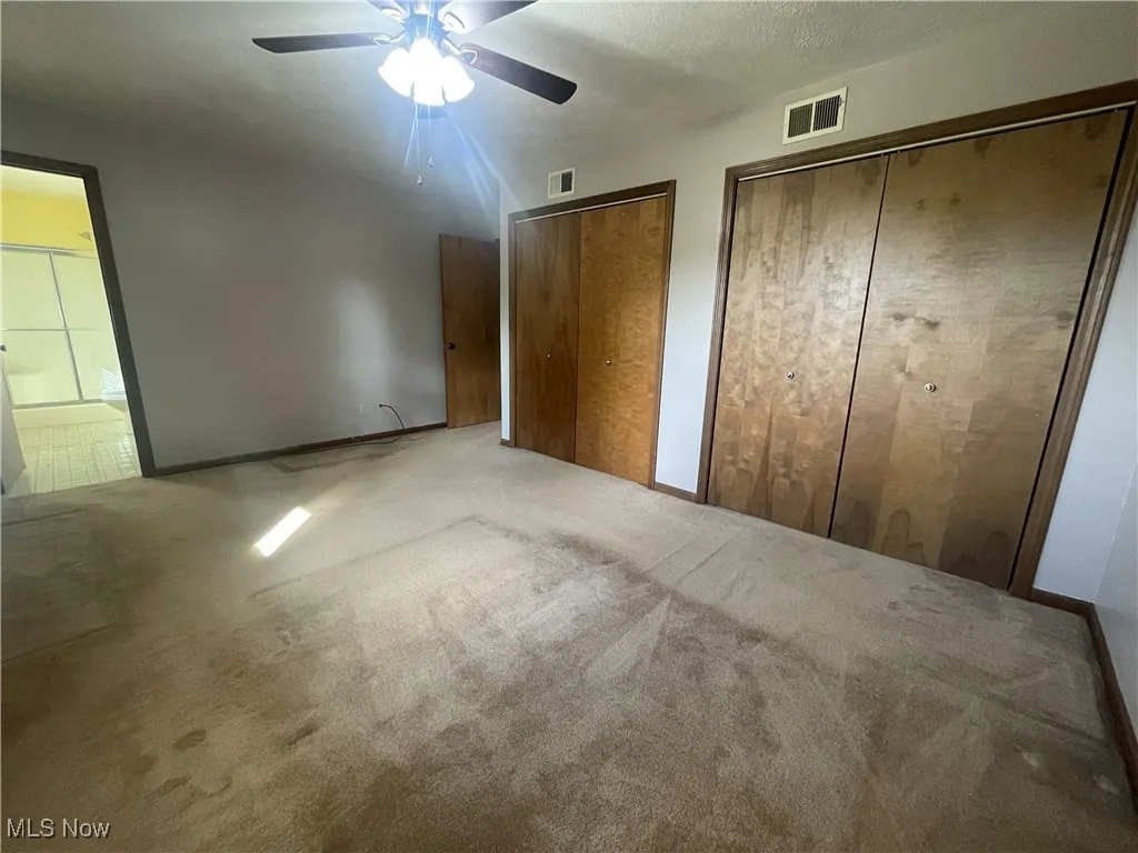 Master bedroom His And Her Closets featuring visible vents, carpet, ceiling fan, and two closets