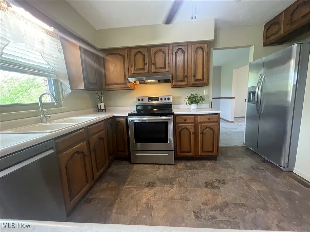 Kitchen featuring under cabinet range hood, appliances with stainless steel finishes, a sink, and light countertops