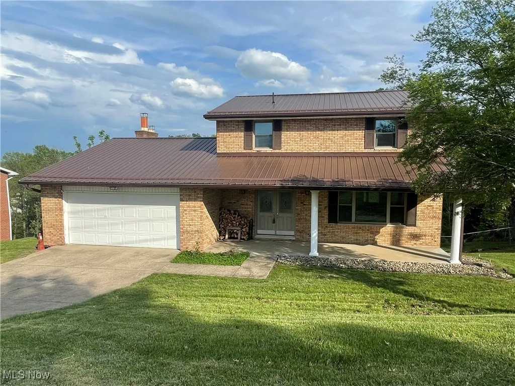 Traditional-style house featuring an attached garage, brick siding, a front yard, concrete driveway, and metal roof