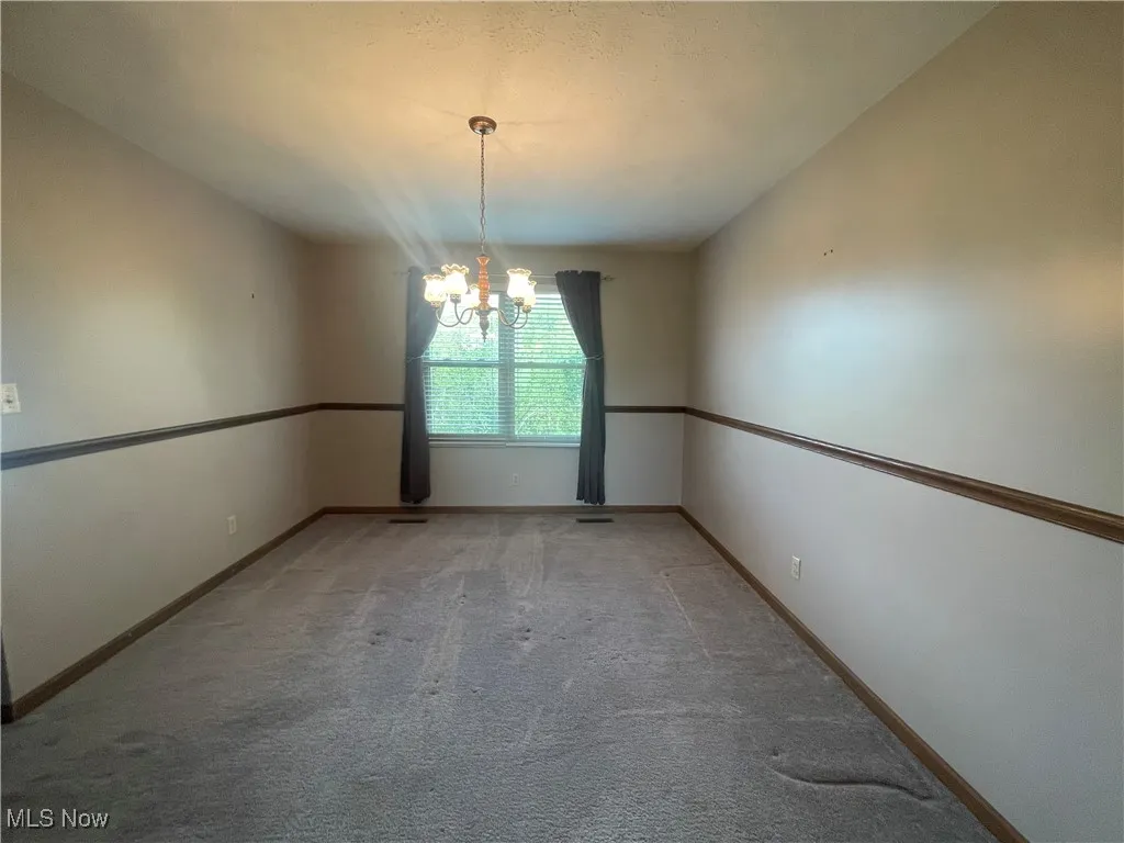 Unfurnished room with baseboards, an inviting chandelier, and light carpet