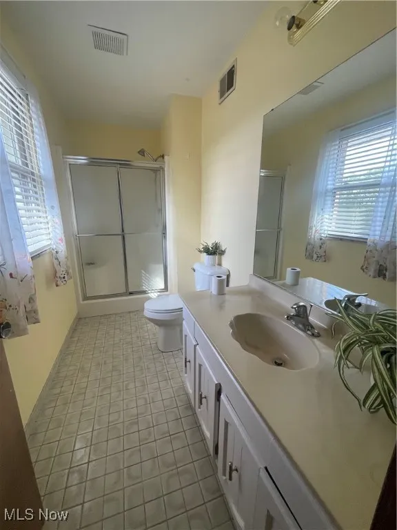 Bathroom with visible vents, a shower with door, and toilet