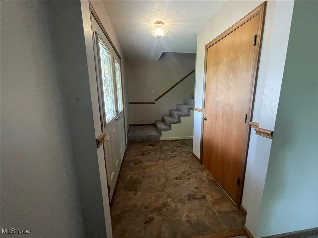 Hallway with baseboards, stone finish floor, and stairway