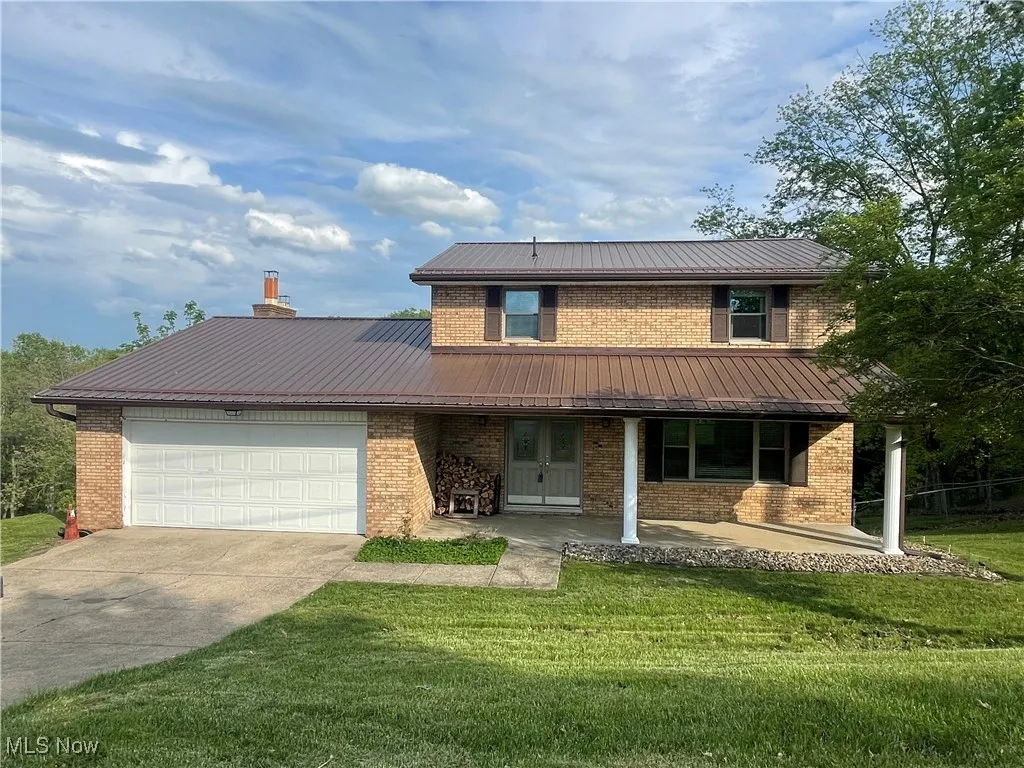 Traditional-style home featuring a front lawn, metal roof, brick siding, concrete driveway, and an attached garage