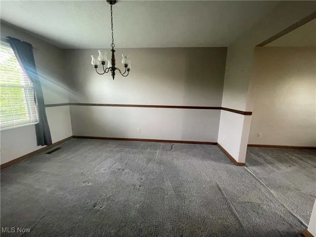  room with carpet floors, baseboards, an inviting chandelier, and visible vents