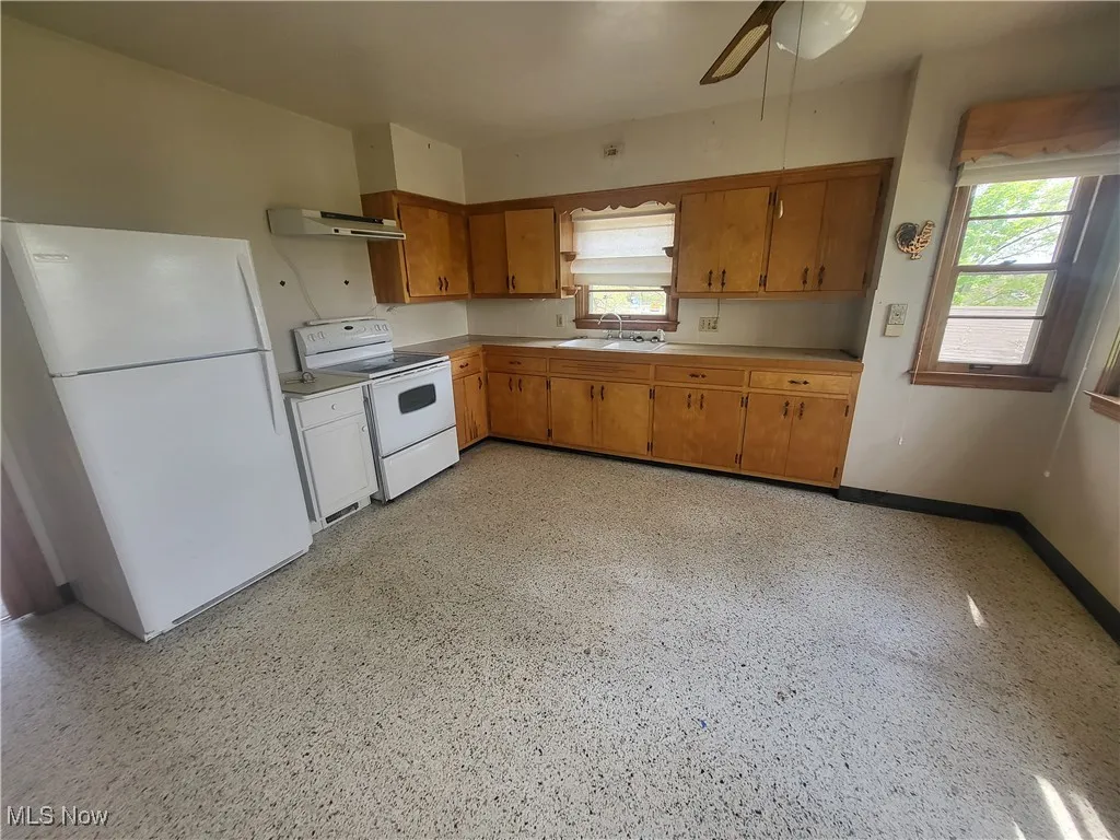 Kitchen featuring ceiling fan, brown cabinets, light countertops, under cabinet range hood, and white​​‌​​​​‌​​‌‌​‌‌​​​‌‌​‌​‌​‌​​​‌​​ appliances