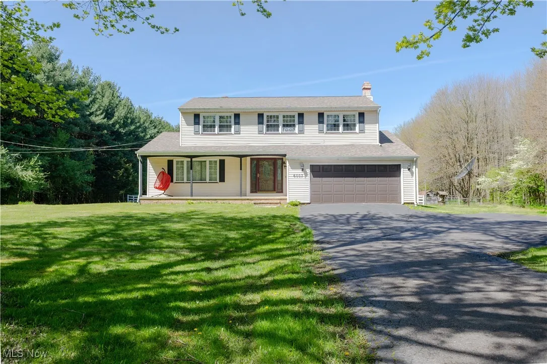 Traditional-style home with a porch, driveway, a chimney, a front lawn, and an attached garage