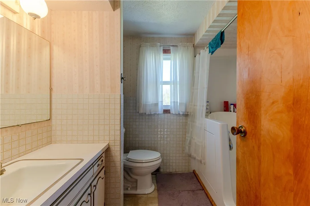 Bathroom featuring vanity, toilet, a wainscoted wall, wallpapered walls, and tile walls