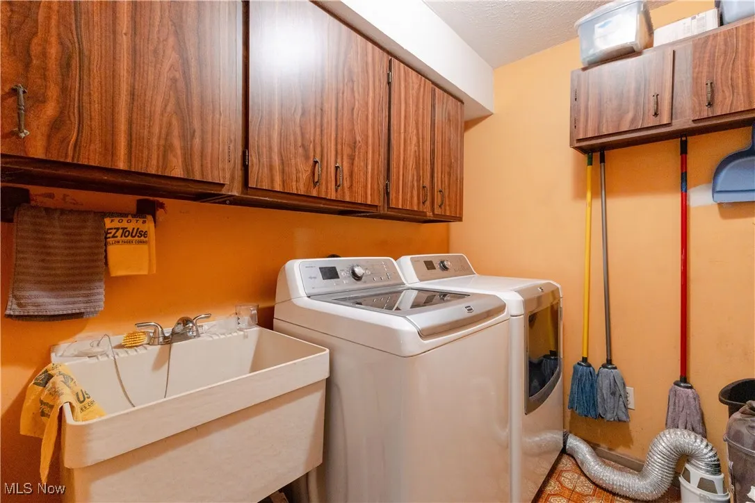 Clothes washing area featuring a sink, washer and clothes dryer, and cabinet space