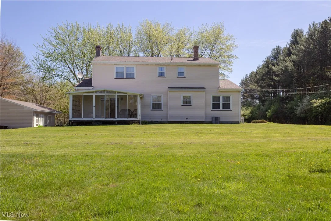 Back of property with a sunroom, central AC unit, a lawn, and a chimney
