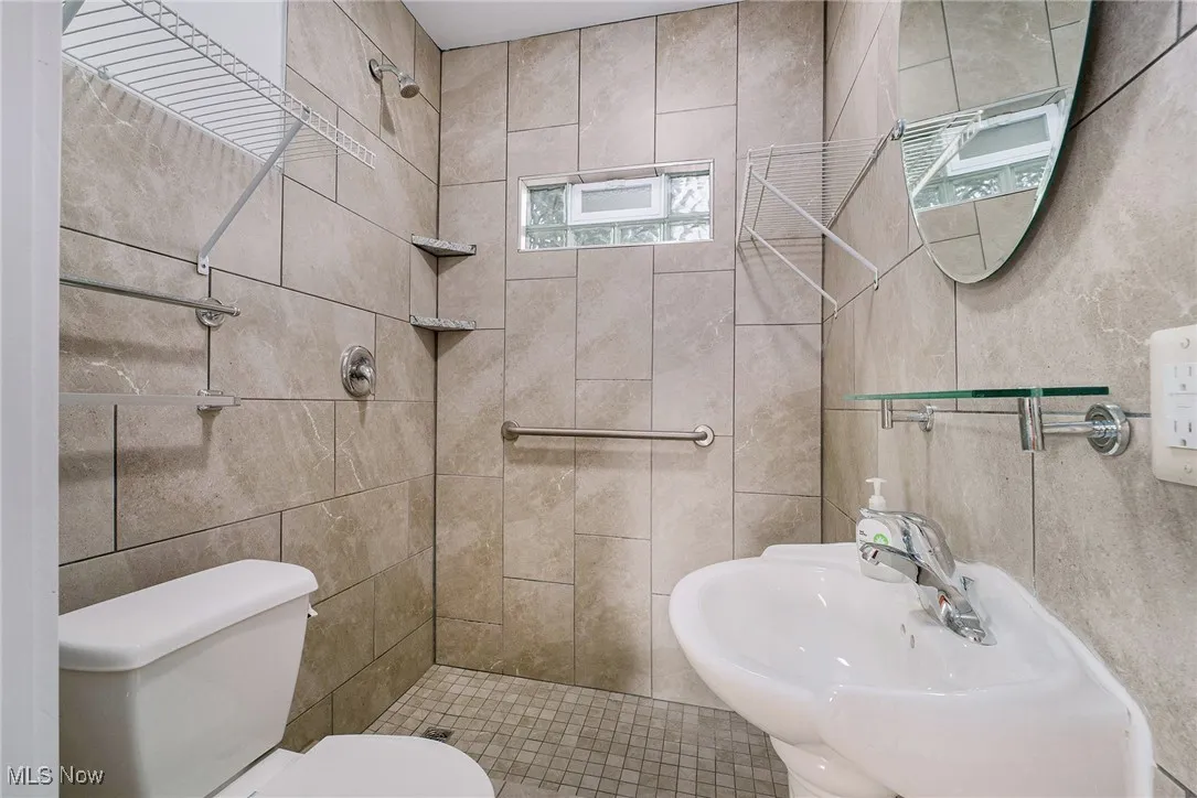 Bathroom featuring a sink, toilet, tiled shower, and tile walls