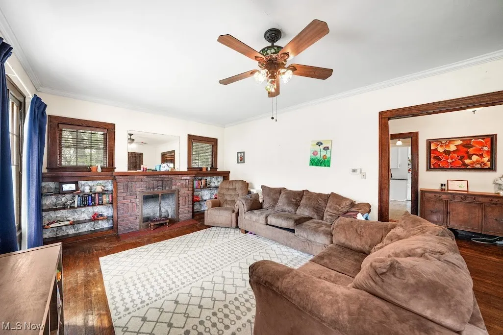 Living room with ornamental molding, a brick fireplace, ceiling fan, and dark wood finished floors