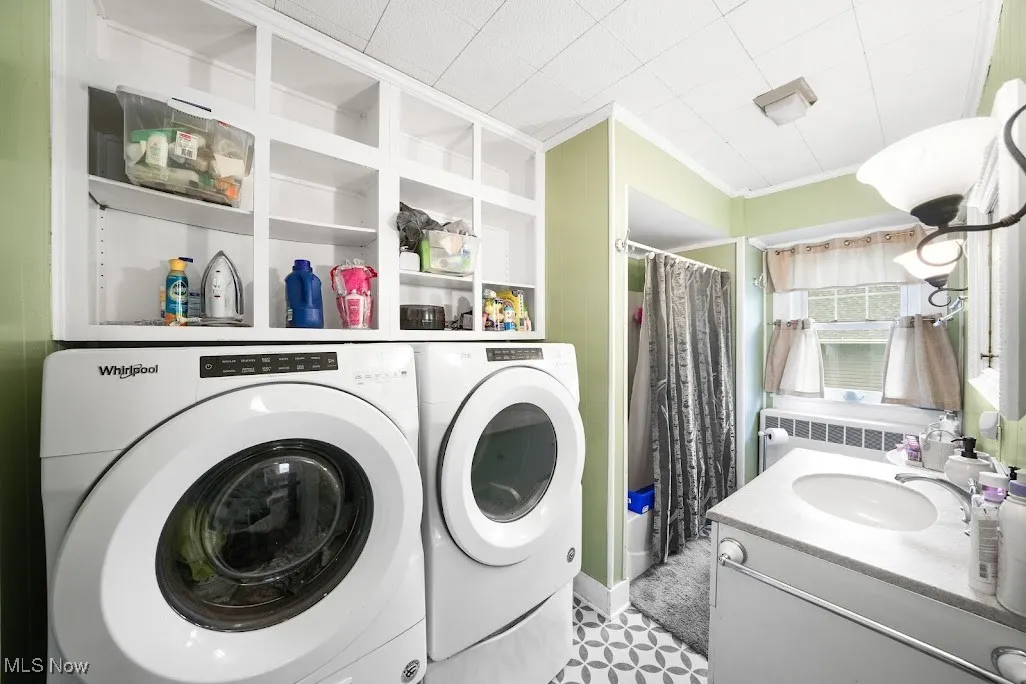 Clothes washing area with laundry area, crown molding, a sink, radiator heating unit, and washer and clothes dryer