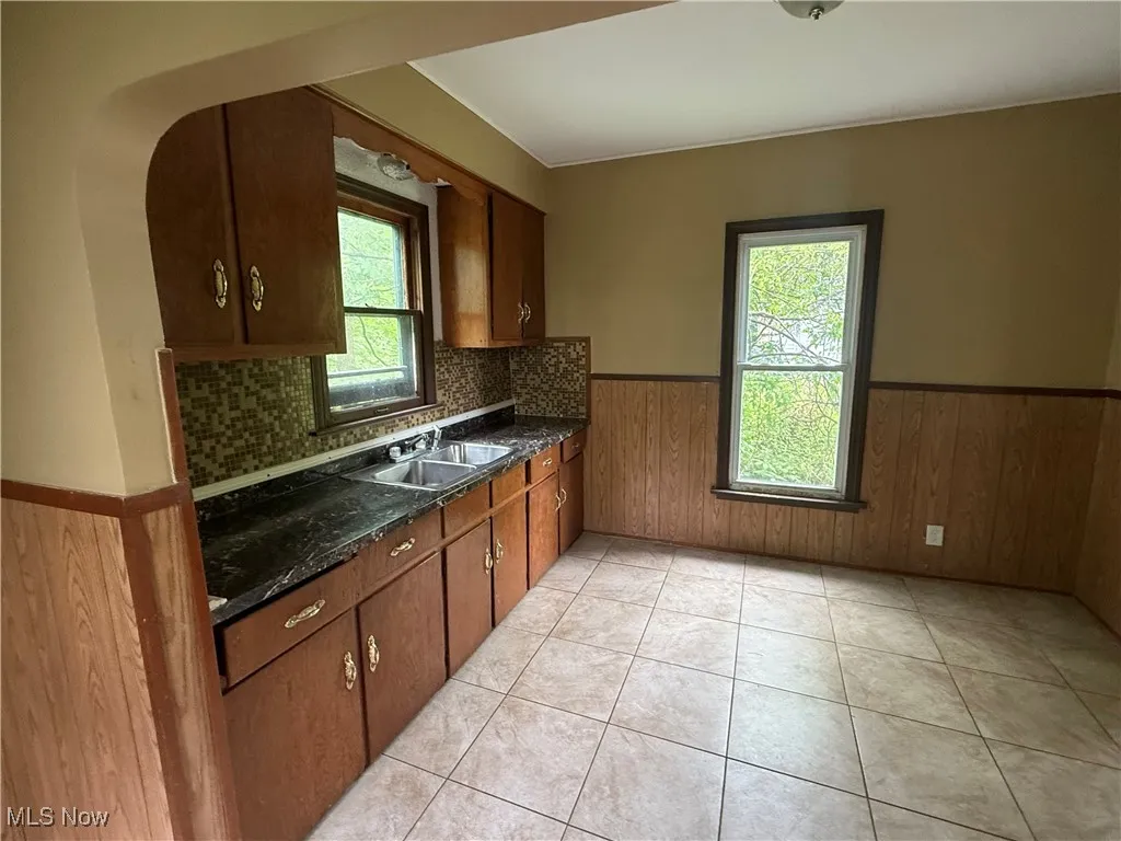 Kitchen with wainscoting, plenty of natural light, light tile patterned floors, wood walls, and dark stone counters