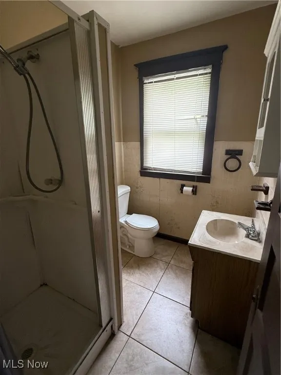 Bathroom featuring a stall shower, tile patterned flooring, vanity, and wainscoting