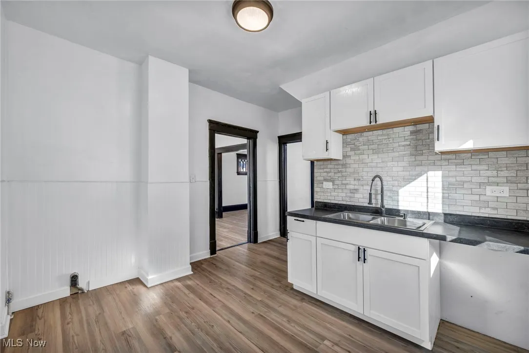 Kitchen featuring dark countertops, white cabinets, a sink, and wood finished floors