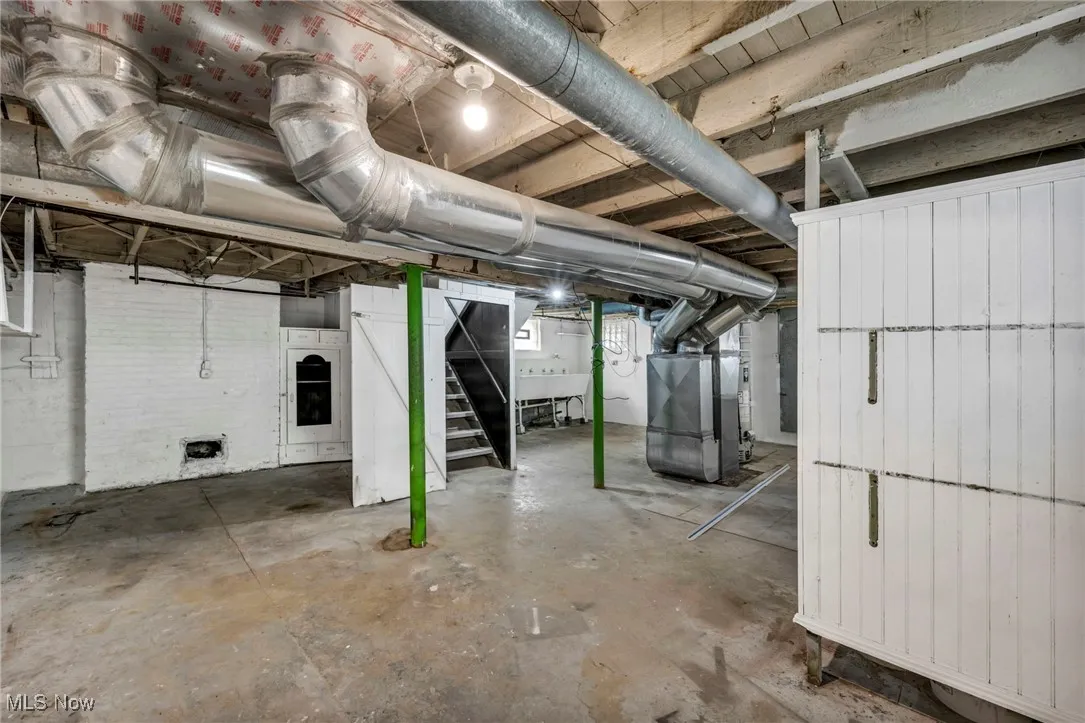 Unfinished basement featuring heating unit, stairs, and a sink
