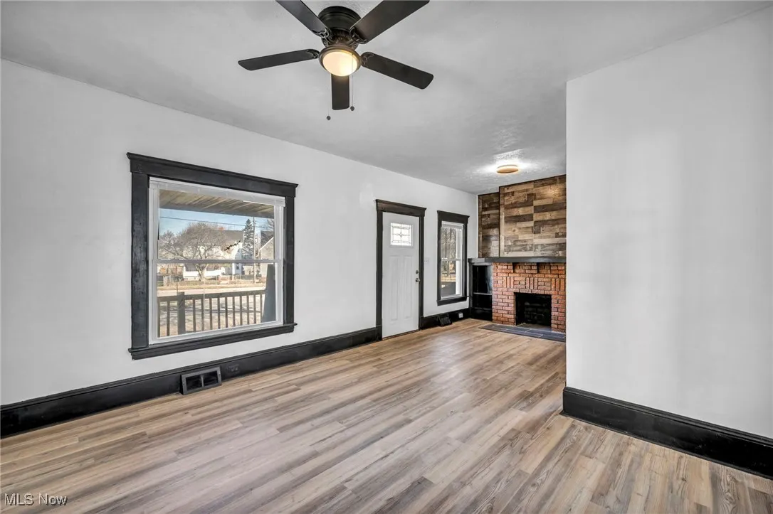 Unfurnished living room with a brick fireplace, visible vents, baseboards, and wood finished floors